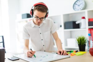A young man with glasses and headphones draws a marker on the magnetic board.